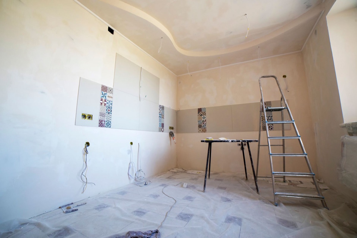 A person on a ladder closely inspecting a long crack in a white drywall ceiling.
