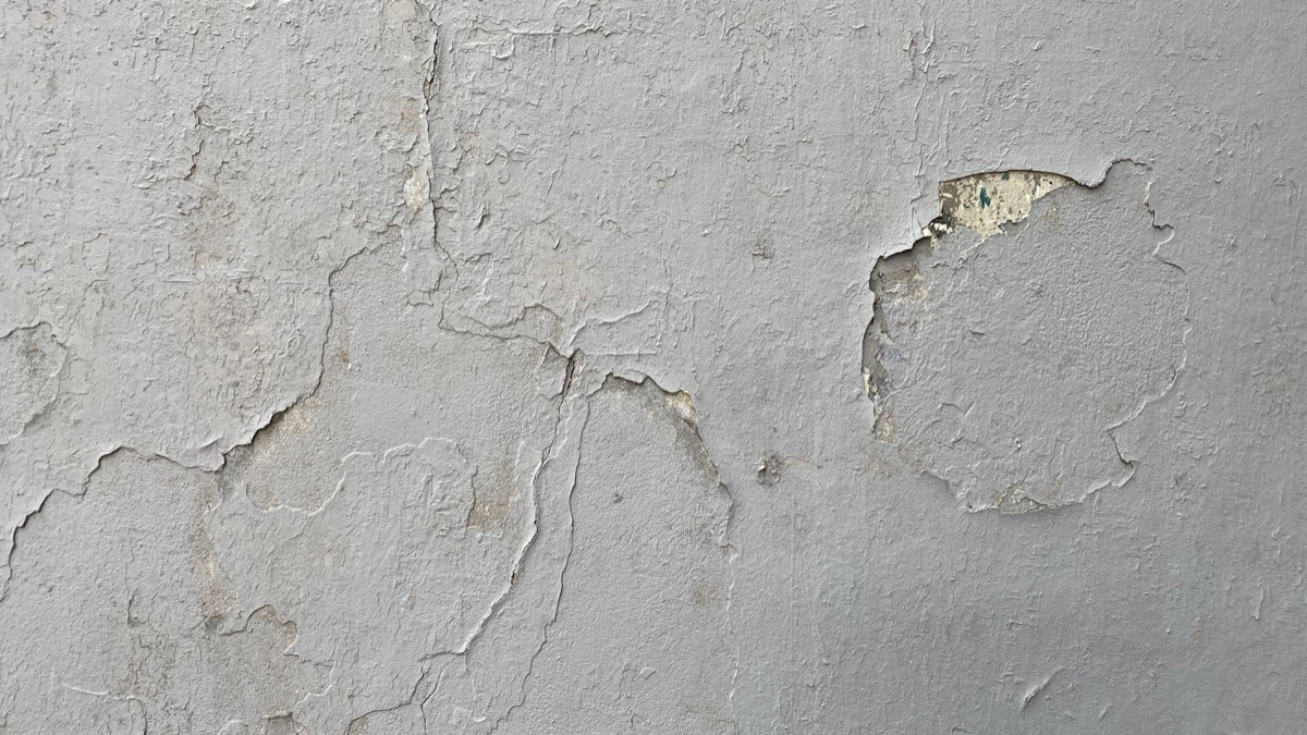 Close-up view of a hairline crack in a white drywall ceiling at the seam with a wall.