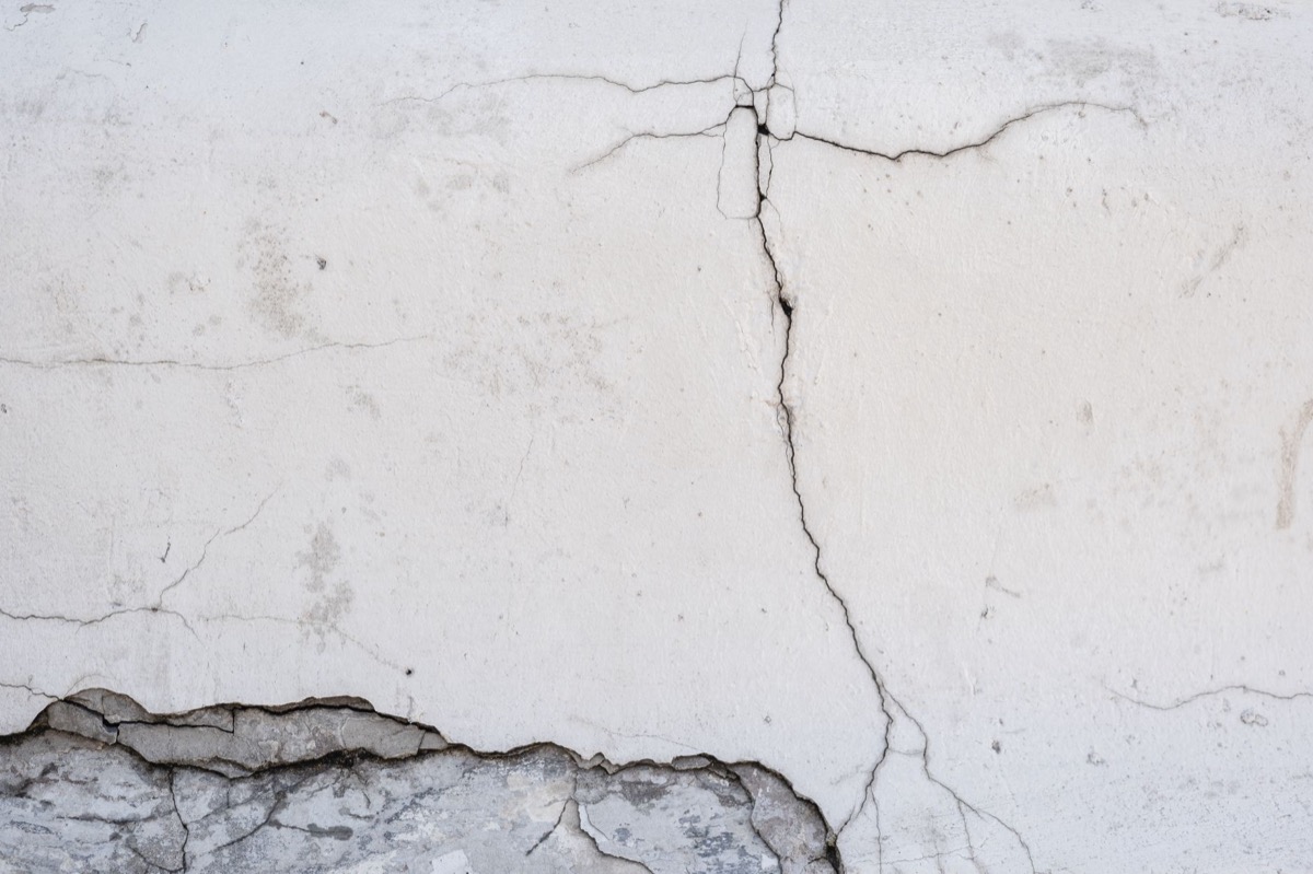 Close-up of a diagonal crack in a white drywall ceiling, showing damage.