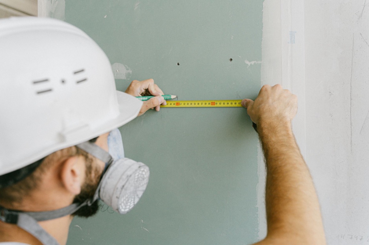 Close-up of a hand using a drywall knife to smooth joint compound over a section of wall where bubbling tape is being repaired.