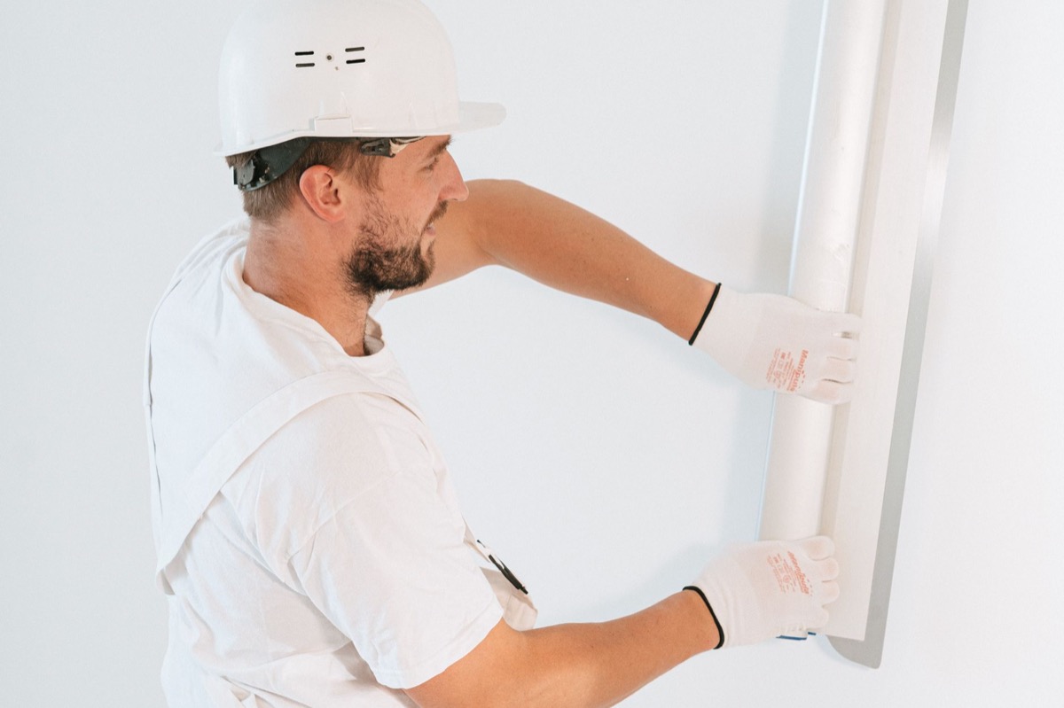 Close-up of a hand applying joint compound over a drywall nail pop repair on a white wall.