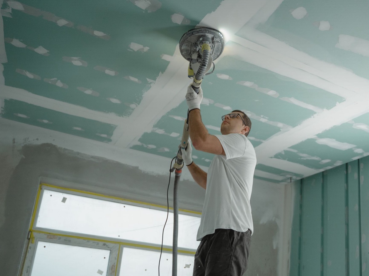 Close-up of a drywall professional inspecting a nail pop with repair tools nearby.